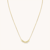 A gold chain necklace from Little Words Project. The necklace includes gold beads that read, TRUST.