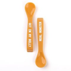 A set of 2 baby spoons in the color orange. One spoon reads, "Meal Monster." The other spoon reads, "Get In My Belly." This spoon set comes from the brand Bella Tunno.