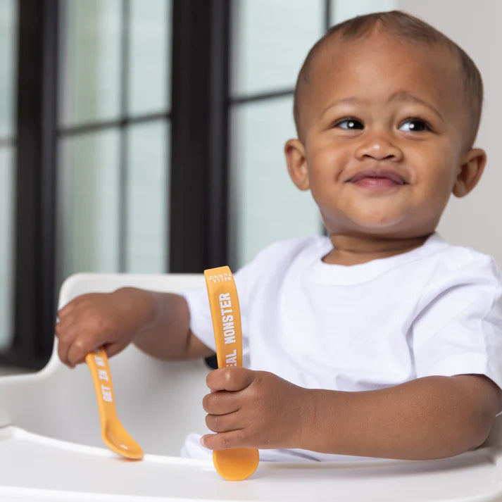 A set of 2 baby spoons in the color orange. One spoon reads, "Meal Monster." The other spoon reads, "Get In My Belly." This spoon set comes from the brand Bella Tunno.