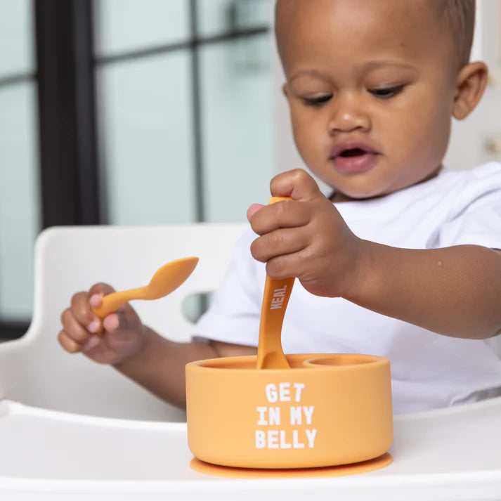 A set of 2 baby spoons in the color orange. One spoon reads, "Meal Monster." The other spoon reads, "Get In My Belly." This spoon set comes from the brand Bella Tunno.