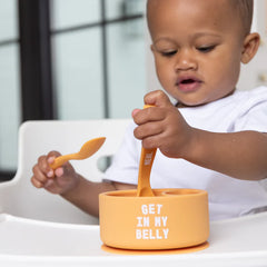 A set of 2 baby spoons in the color orange. One spoon reads, "Meal Monster." The other spoon reads, "Get In My Belly." This spoon set comes from the brand Bella Tunno.