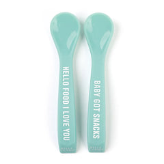 A set of 2 baby spoons in the color teal blue. One spoon reads, "Hello Food I Love You." The other spoon reads, "Baby Got Snacks." This spoon set comes from the brand Bella Tunno.