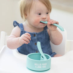 A set of 2 baby spoons in the color teal blue. One spoon reads, "Hello Food I Love You." The other spoon reads, "Baby Got Snacks." This spoon set comes from the brand Bella Tunno.