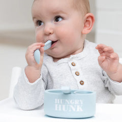 A set of 2 baby spoons in the color blue. One spoon reads, "Hungry Hunk." The other spoon reads, "Stud Muffin." This spoon set comes from the brand Bella Tunno.