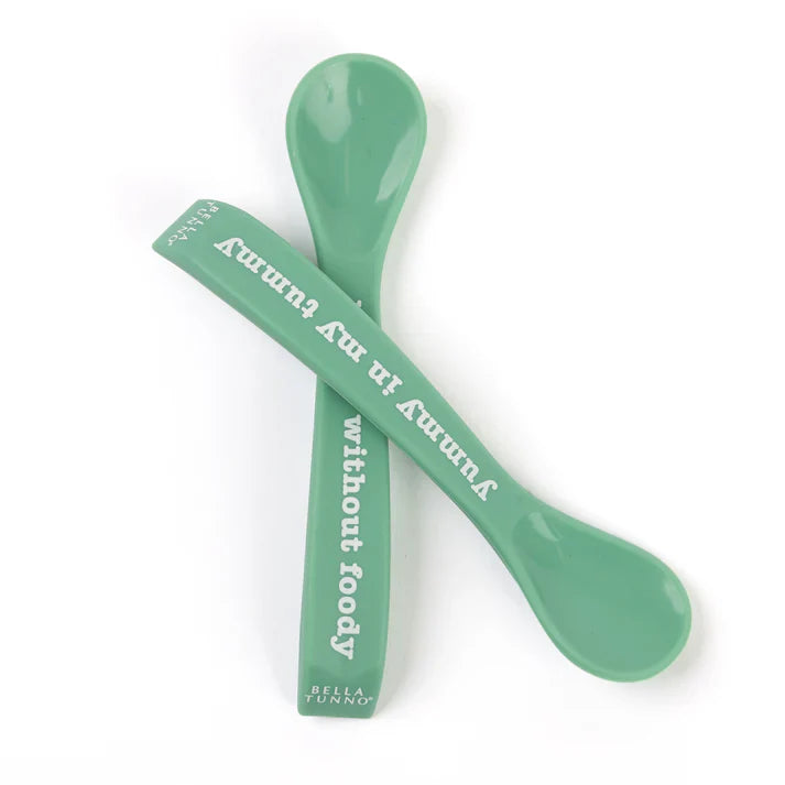 A set of 2 baby spoons in the color green. One spoon reads, "Yummy in my tummy." The other spoon reads, "moody without foody." This spoon set comes from the brand Bella Tunno.