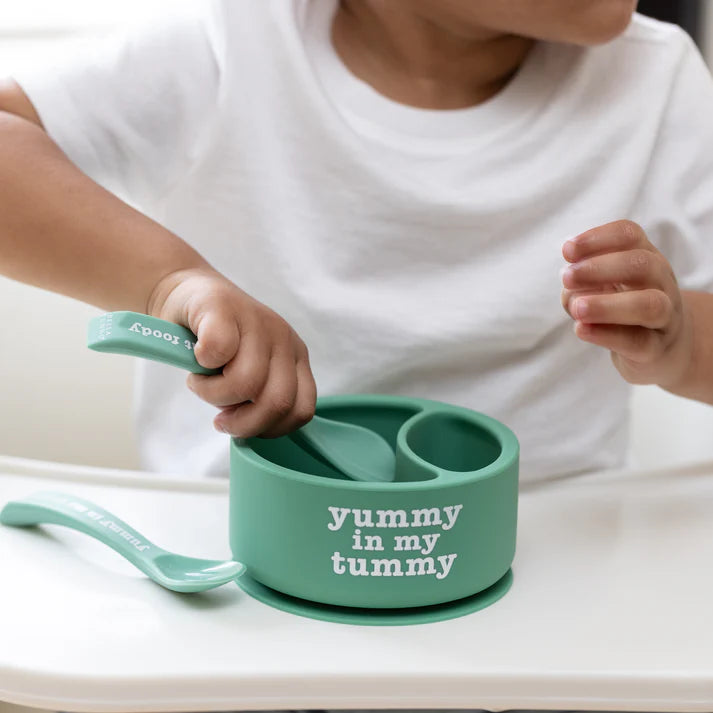 A set of 2 baby spoons in the color green. One spoon reads, "Yummy in my tummy." The other spoon reads, "moody without foody." This spoon set comes from the brand Bella Tunno.