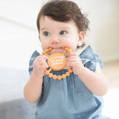 Orange color Happy Teether that reads, "I LAUGH AT DAD JOKES" in the middle. The teether is made from silicone, and comes from the brand Bella Tunno.