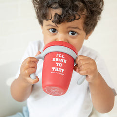 A red color sippy cup, with gray handles. The sippy cup reads, "I'll Drink To That" with the Bella Tunno logo at the bottom.