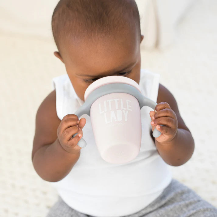 A pink color sippy cup, with gray handles. The sippy cup reads, "Little Lady" with the Bella Tunno logo at the bottom.