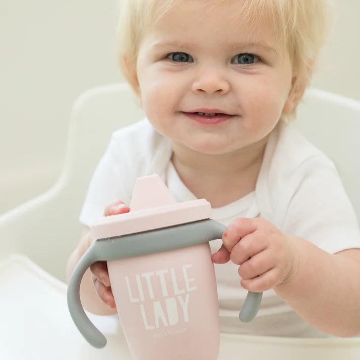 A pink color sippy cup, with gray handles. The sippy cup reads, "Little Lady" with the Bella Tunno logo at the bottom.