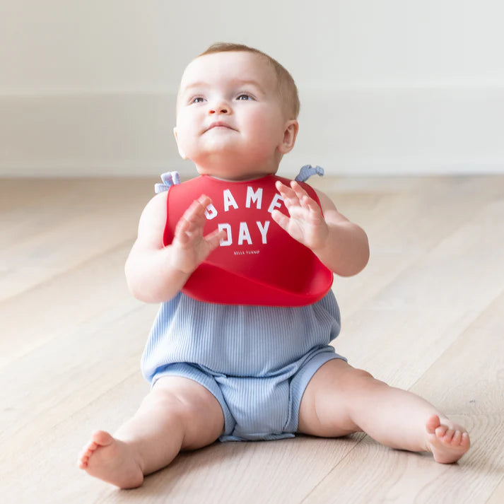 Red color Wonder Bib that reads, "Game Day" with the Bella Tunno logo below it. The bib is adjustable in size with 4 snaps that easily fit around the neck. The Wonder Bib is designed out of silicone, and is made by Bella Tunno.