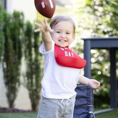 Red color Wonder Bib that reads, "Game Day" with the Bella Tunno logo below it. The bib is adjustable in size with 4 snaps that easily fit around the neck. The Wonder Bib is designed out of silicone, and is made by Bella Tunno.