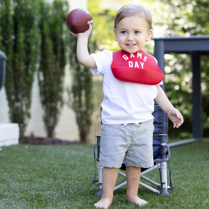 Red color Wonder Bib that reads, "Game Day" with the Bella Tunno logo below it. The bib is adjustable in size with 4 snaps that easily fit around the neck. The Wonder Bib is designed out of silicone, and is made by Bella Tunno.