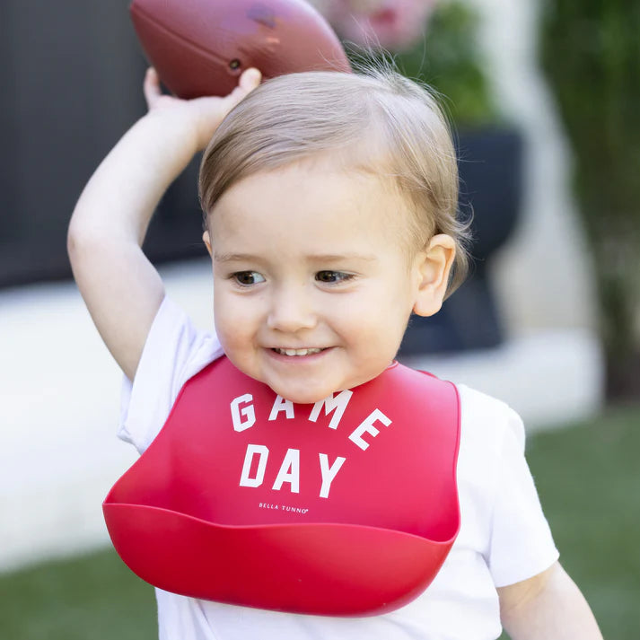 Red color Wonder Bib that reads, "Game Day" with the Bella Tunno logo below it. The bib is adjustable in size with 4 snaps that easily fit around the neck. The Wonder Bib is designed out of silicone, and is made by Bella Tunno.