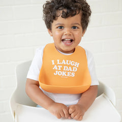 Orange color Wonder Bib that reads, "I Laugh A Dad Jokes" with the Bella Tunno logo below it. The bib is adjustable in size with 4 snaps that easily fit around the neck. The Wonder Bib is designed out of silicone, and is made by Bella Tunno.