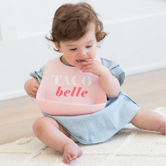 Pink color Wonder Bib that reads, "TACO belle" with the Bella Tunno logo below it. The bib is adjustable in size with 4 snaps that easily fit around the neck. The Wonder Bib is designed out of silicone, and is made by Bella Tunno.