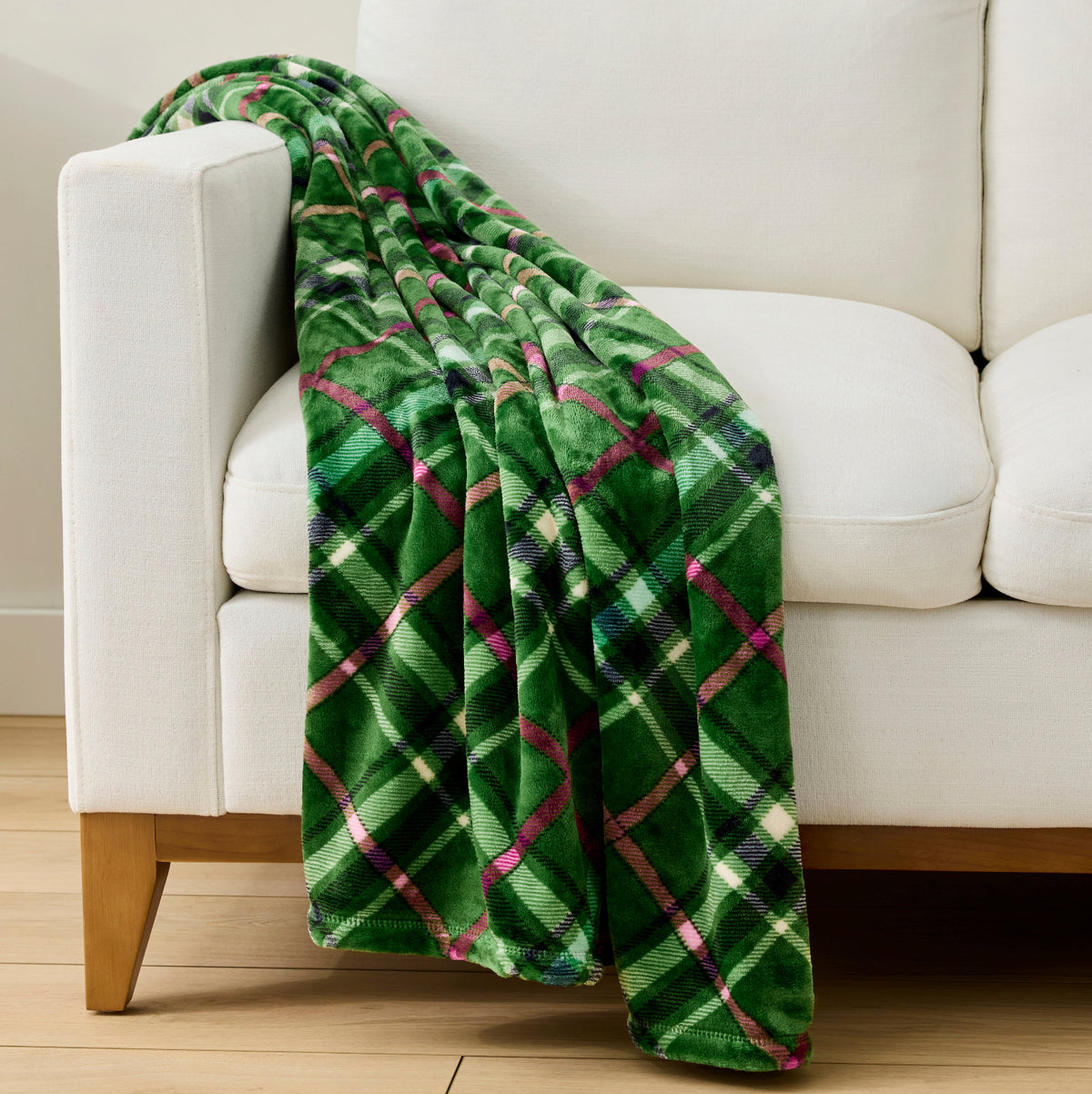 A green plaid throw blanket draped over a white armchair in a bright, modern living room setting.