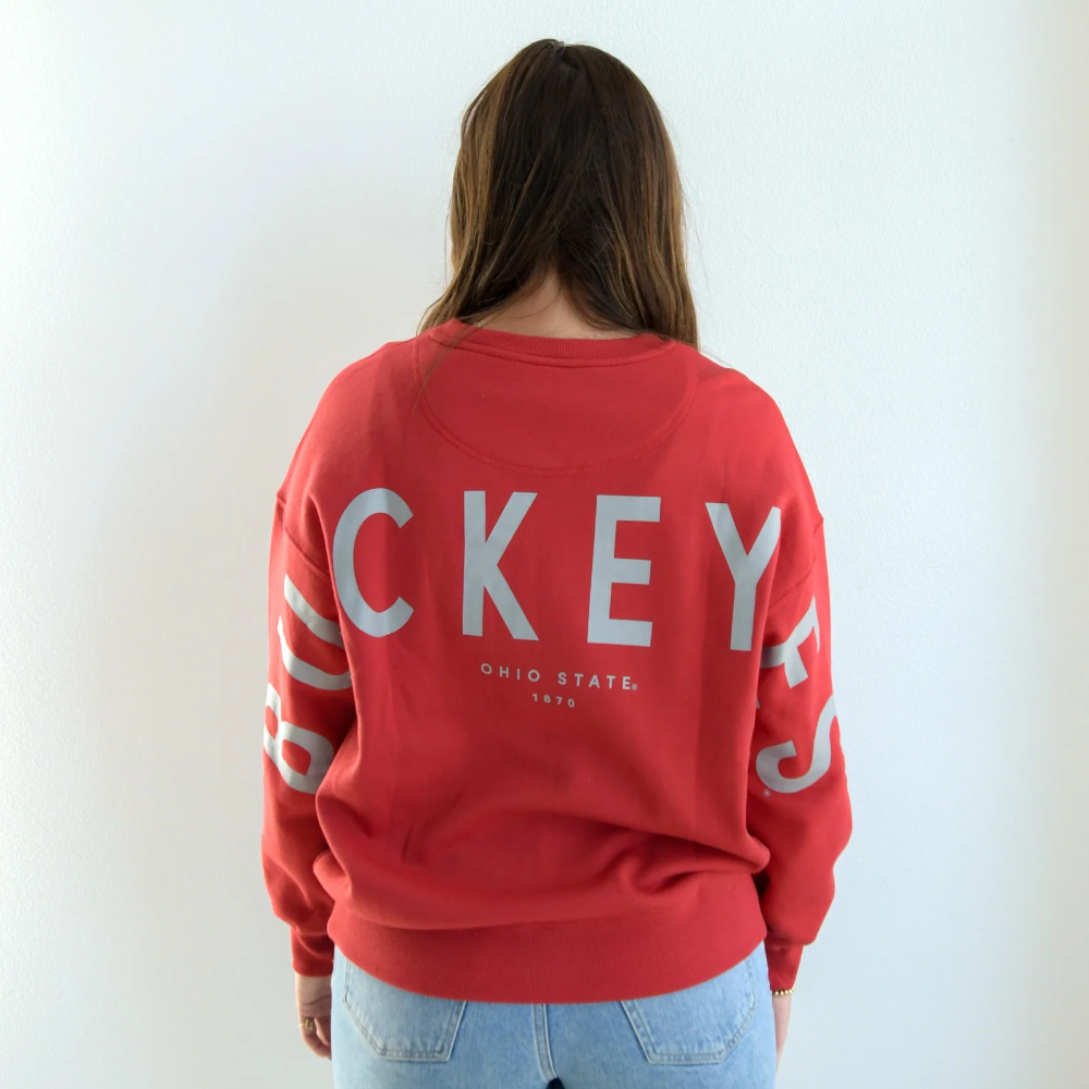 A women with brown hair wearing a red crewneck sweater. On the back of the sweater it reads, "BUCKEYES" in the color grey. The lettering stretches from the left arm, across the entire back to the right arm. Just below the word BUCKEYES shows "Ohio State 1870" also in the color grey.