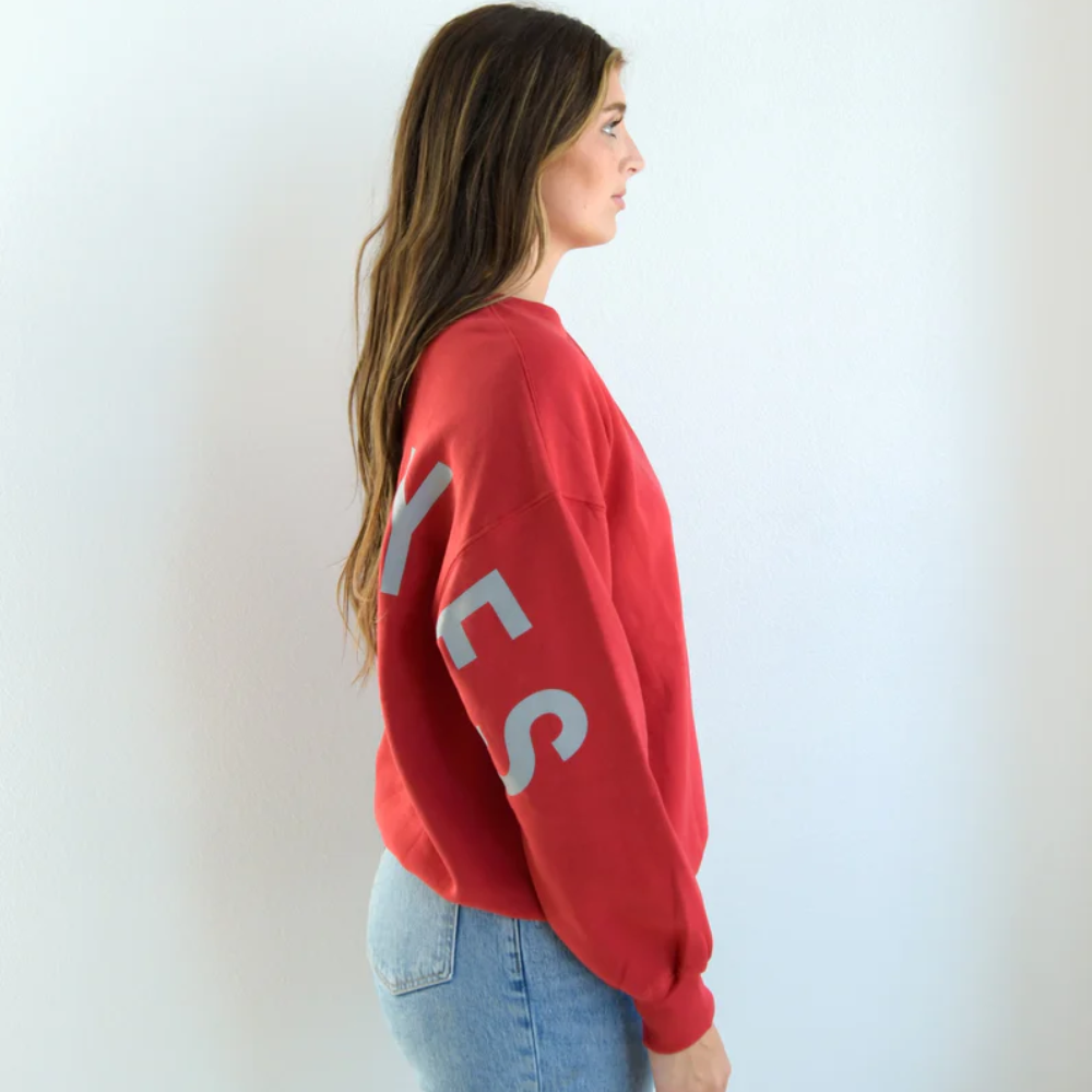 A women wearing a red crewneck sweater, showing the right side arm. With BUCKEYES lettering coming down the right arm in the color grey.