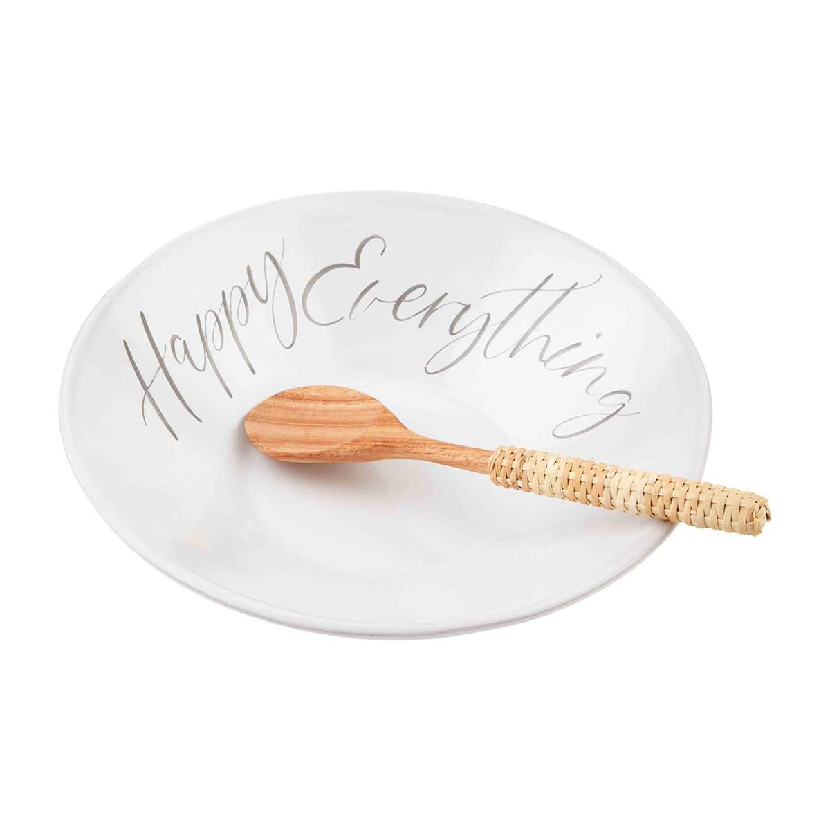 A white bowl that reads "Happy Everything" with a wooden spoon with a rattan-wrapped handle sitting inside the bowl.