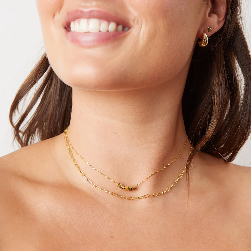 A gold chain necklace from Little Words Project. The necklace includes gold beads that read, TRUST.