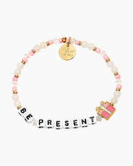 Beaded bracelet in white and pink, with the phrase "Be Present" with a gift wrapped present charm.