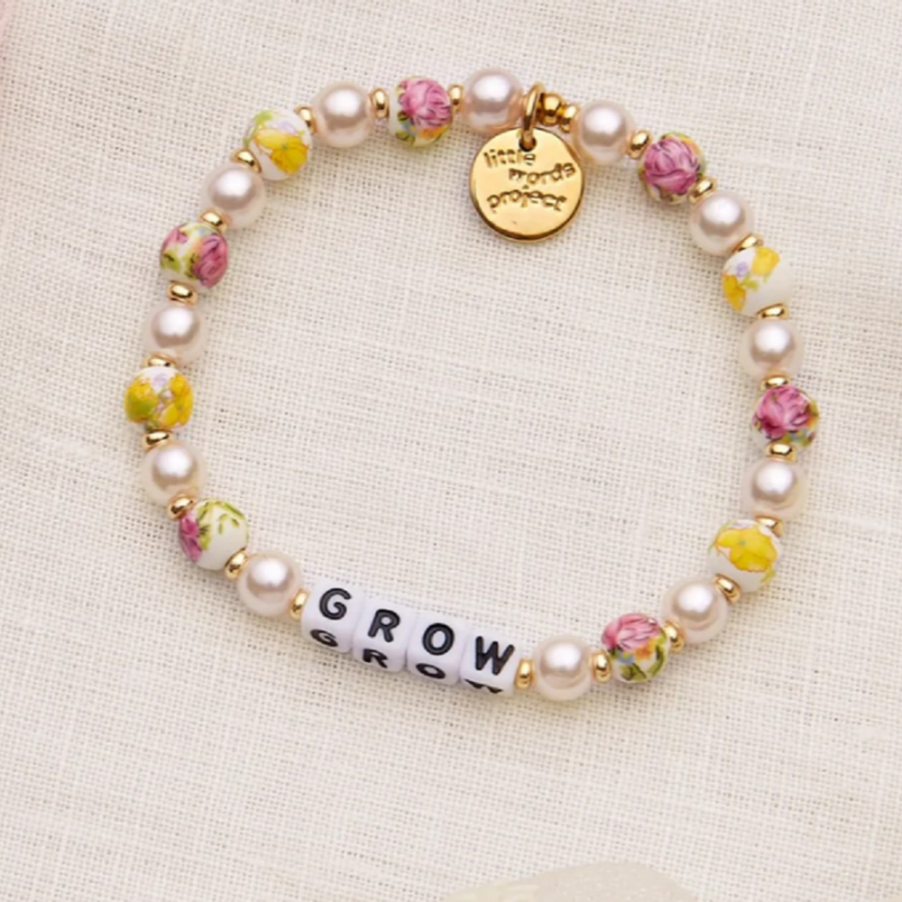 A  gold, pink, and white bead bracelet that says, Grow.