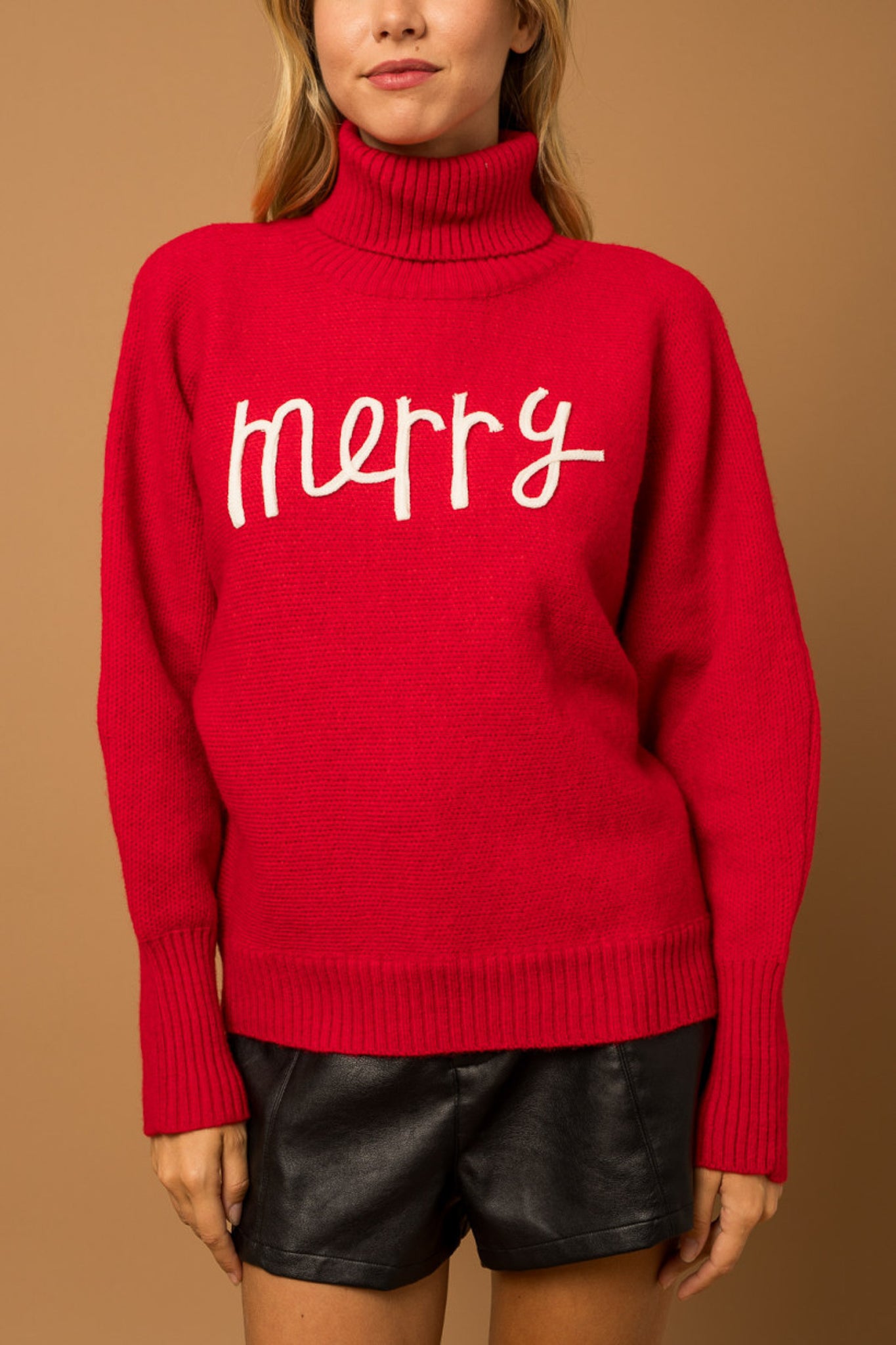 A red turtleneck sweater with the phrase "Merry" in the color white.