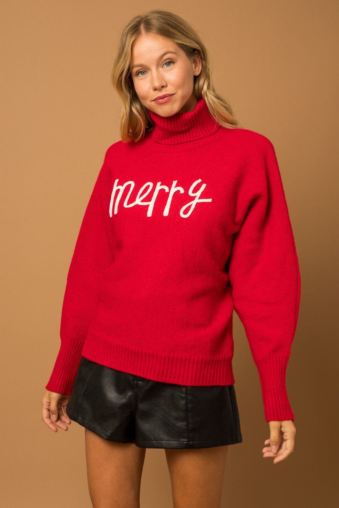 A red turtleneck sweater with the phrase "Merry" in the color white.