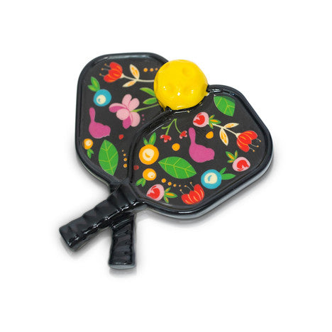 A pair of black Pickleball paddles, with a yellow pickleball from Nora Fleming.