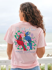 A pink shirt from the brand Simply Southern. With a red cardinal, and a blue jay bird on the back. With the phrase, "Be Still and Know."