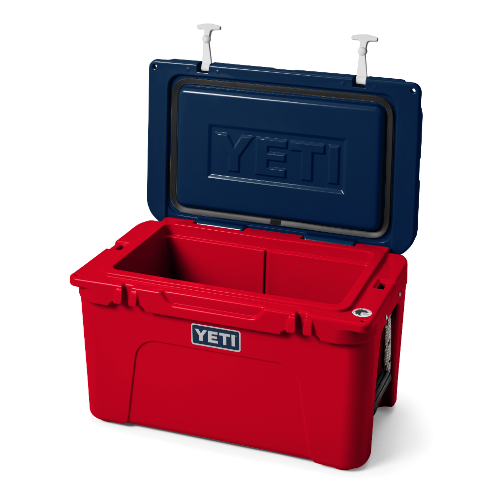 The limited edition 2024 Tundra 45 YETI Cooler with the lid open. The lid is the color navy blue, showing a YETI logo also in navy blue engraved into the interior of the lid. The base of the cooler is red, and the secure straps on the lid are white. The front of the cooler showcases a classic YETI logo.