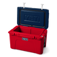 The limited edition 2024 Tundra 45 YETI Cooler with the lid open. The lid is the color navy blue, showing a YETI logo also in navy blue engraved into the interior of the lid. The base of the cooler is red, and the secure straps on the lid are white. The front of the cooler showcases a classic YETI logo.