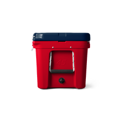 A side view of the limited edition YETI Tundra 45 in Patriotic Red, White, and Blue. The top lid is navy blue, the base of the cooler is red, and the handles on the side are white, with a black hand grip. There is a number 45 engraved into the side of the cooler, also in the color red. The water drain on the cooler is the color black.