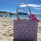 A baby Bogg® Bag chillin' in the sand, full of beach supplies with a curse ship in the background. (This could be you, buy a Bogg® today!)
