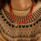 Model wearing the red BaubleBar Janette Beaded Ring Necklace layered with other necklaces over a patterned knit sweater.