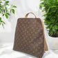 Beaudin Riley bronze backpack with full monogram front displayed beside plants