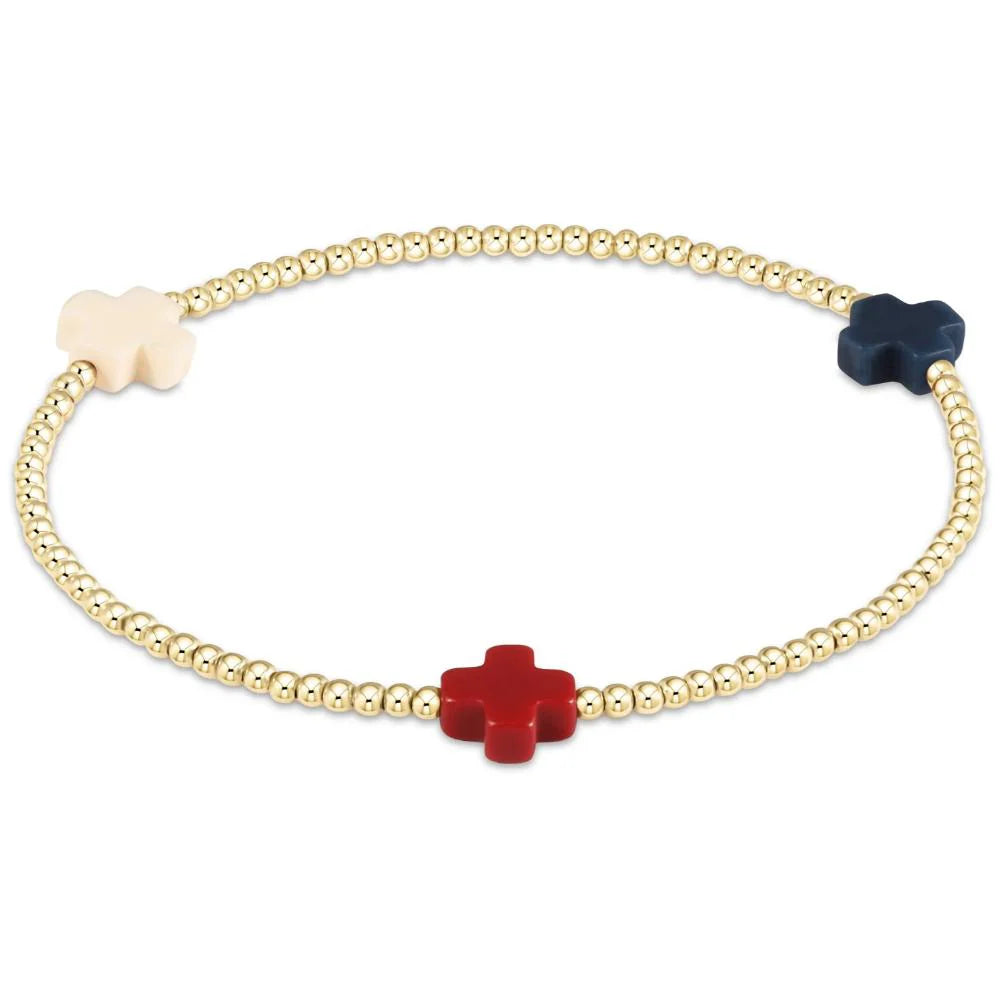 A gold enewton bracelet with a red, white, and blue cross.