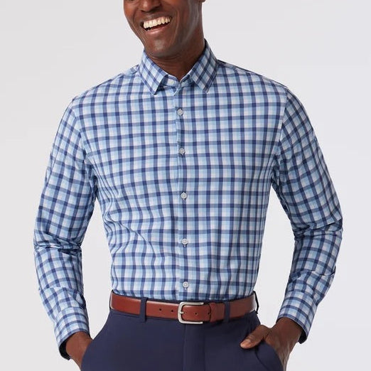 A man wearing a blue and white checkered long-sleeve button-down shirt, navy blue trousers, and a brown leather belt, standing against a light gray studio background.
