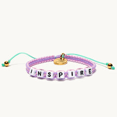 A woven bracelet that's purple and turquoise with the word 'inspire'.