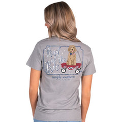 Back view of a Simply Southern Women's Land of the Free Short Sleeve Tee on a model. Showing a Golden Doodle sitting in a little red wagon, while wearing an American flag bow tie.