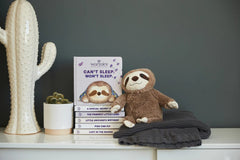 A stuffed sloth sitting next to the book on a book shelf.
