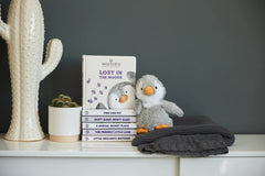 A stuffed animal penguin sitting next to the book on a shelf.