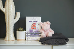 A stuffed animal pink pig sitting next to the book on a shelf.